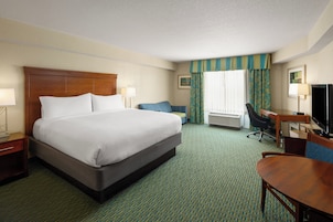 A hotel room with a large bed, a desk with a chair, a television, and a window with curtains.