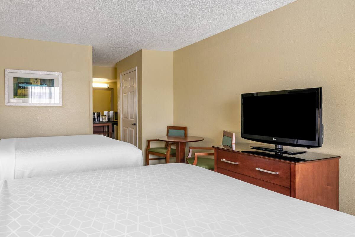 A hotel room with two beds, a television on a wooden cabinet, a small table with chairs, and a framed picture on the wall.