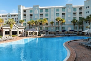 A hotel pool area with lounge chairs and umbrellas, surrounded by palm trees and a multi-story building with balconies. - Holiday Inn Resort Orlando - Lake Buena Vista by IHG (Orlando)