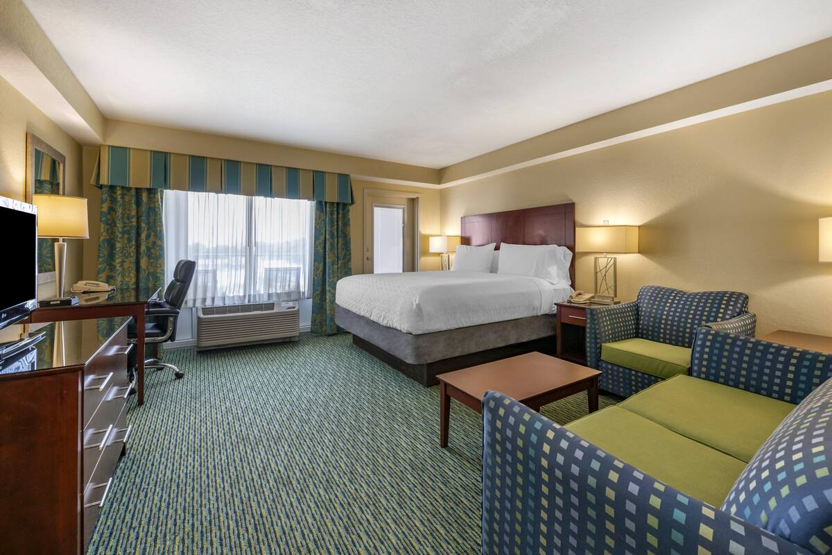 A hotel room with a bed, a desk, a chair, a sofa, and a television.