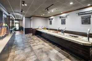 Zona de buffet con diversas opciones de comida, incluyendo una sección para fruta y yogur.
