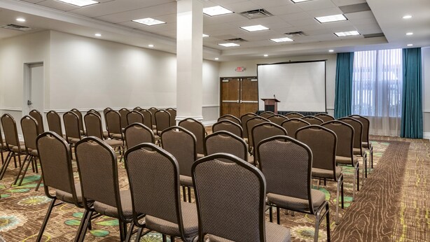 A conference room with rows of chairs, a podium, a projection screen, and a carpeted floor. - Holiday Inn Resort Orlando - Lake Buena Vista by IHG (Orlando)