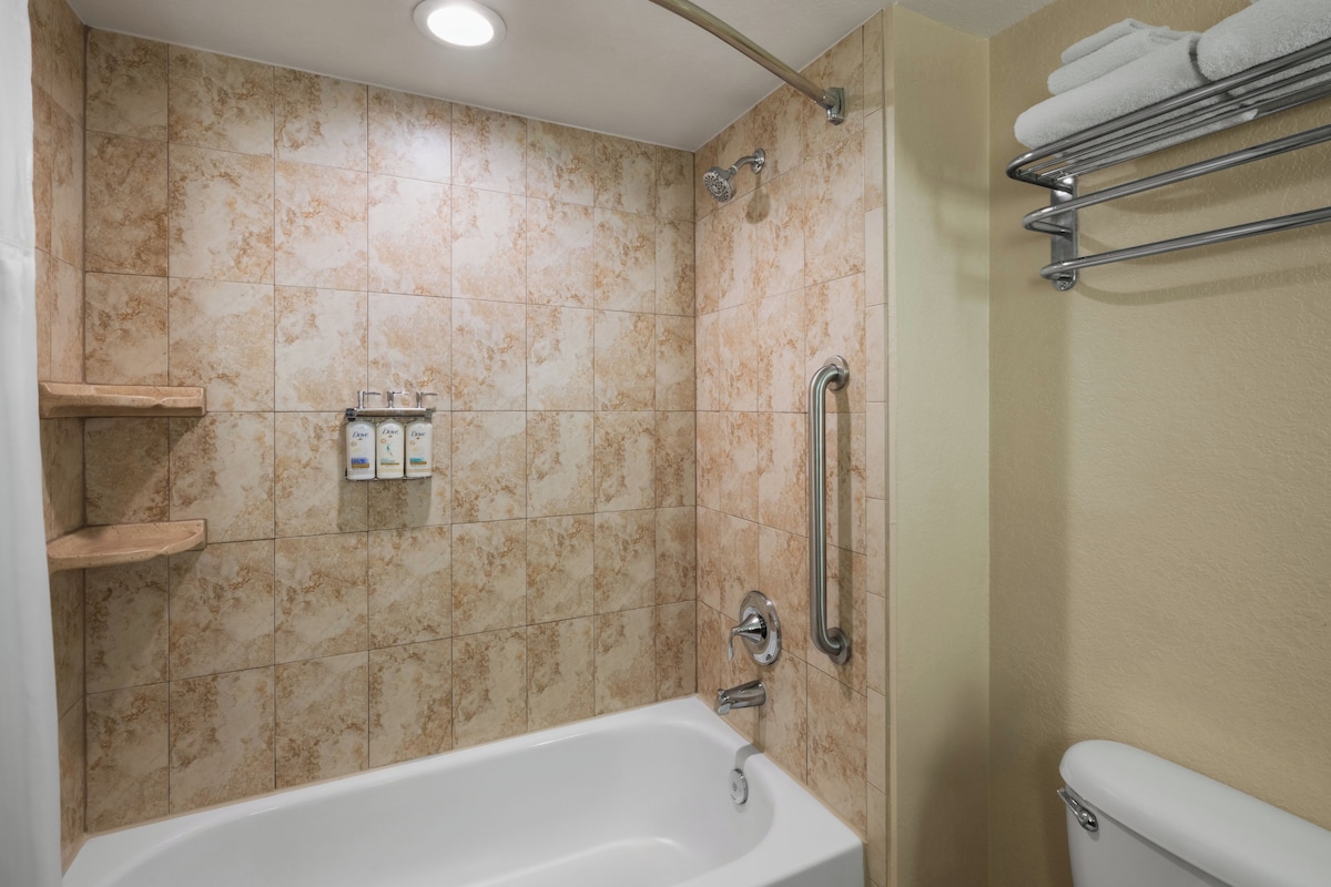 A bathroom with a bathtub, a shower, and a toilet. There are shelves with toiletries and a towel rack.