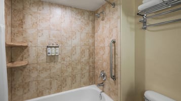 A bathroom with a bathtub, a shower, and a toilet. There are shelves with toiletries and a towel rack.