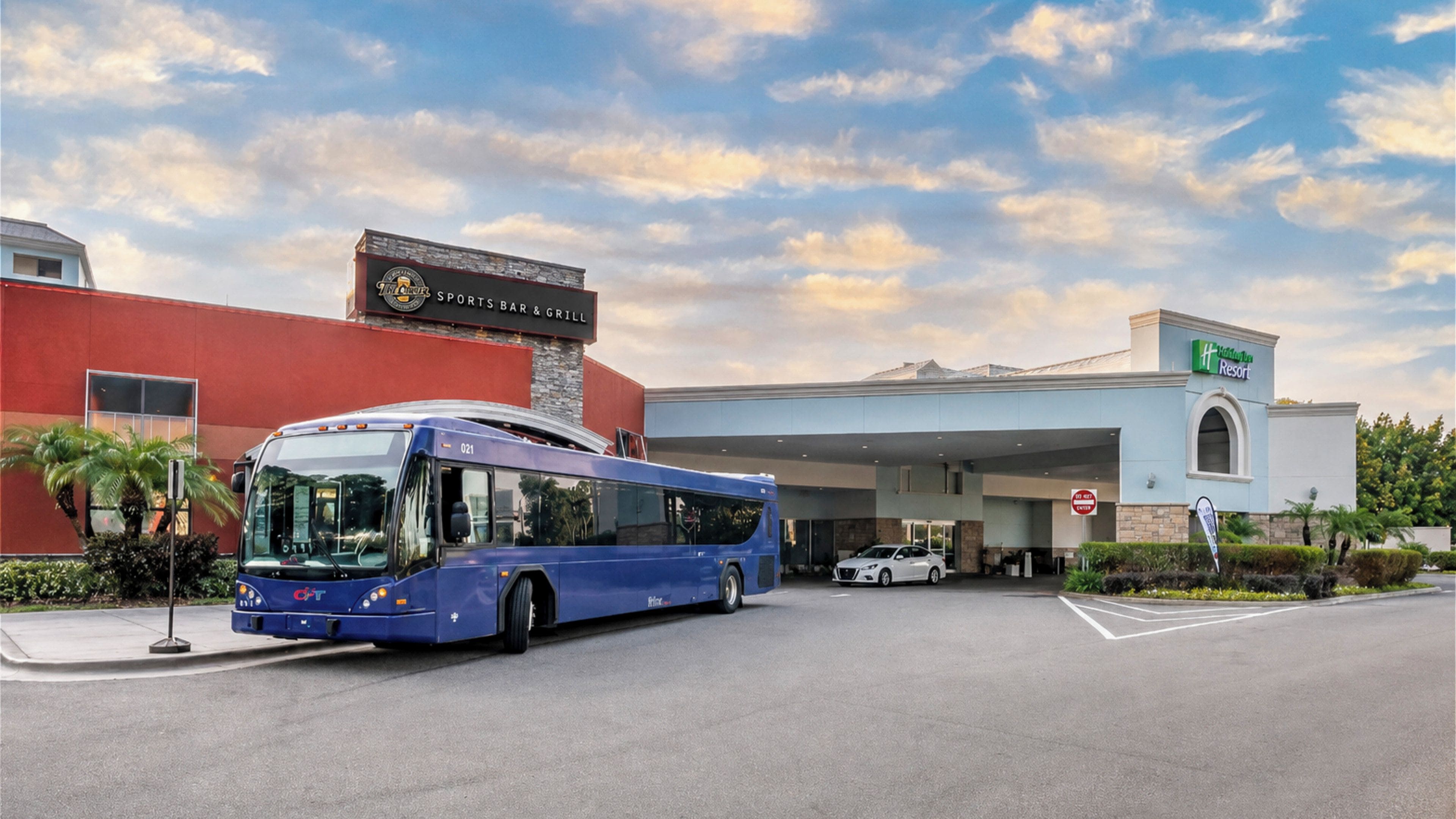 A bus parked in front of a hotel with a sports bar and grill sign.