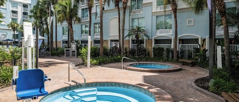 Un área de piscina con dos piscinas circulares, rodeada de palmeras y un edificio de varios pisos con balcones.