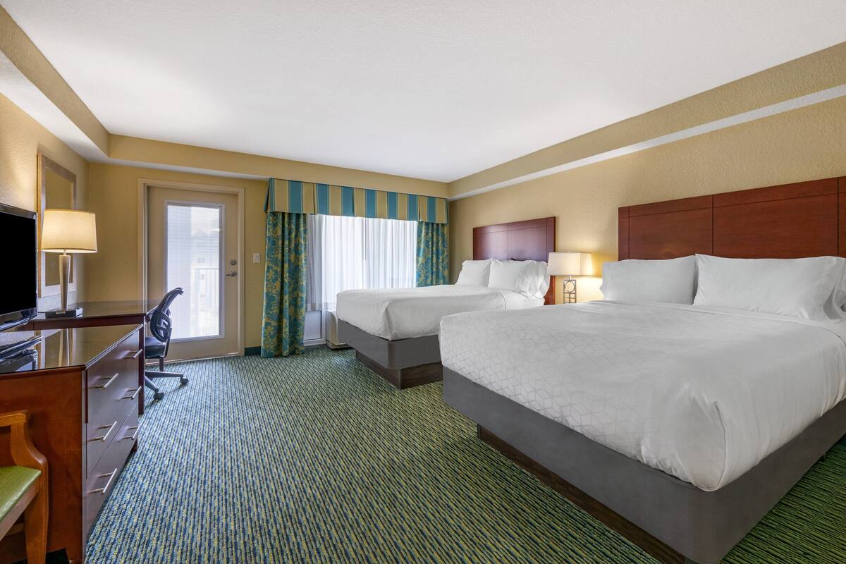 A hotel room with two beds, a desk with a chair, a television, and a window with curtains.