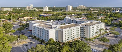 A multi-story hotel with a central courtyard, surrounded by parking and greenery.