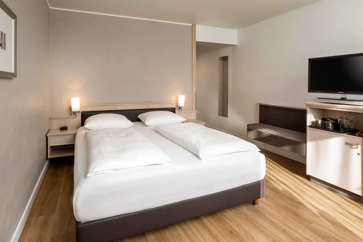 A hotel room with a large bed, bedside tables, a TV, and a minibar.