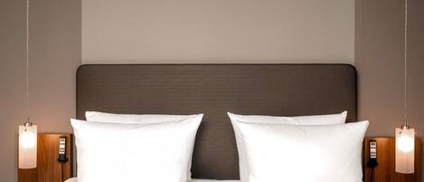 Una cama doble con cabecera oscura, dos lámparas de noche y una mesita de noche de madera.