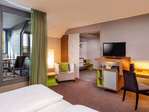Une chambre d’hôtel comprenant un lit, un bureau avec une télévision, une chaise, un canapé et une fenêtre avec des rideaux.