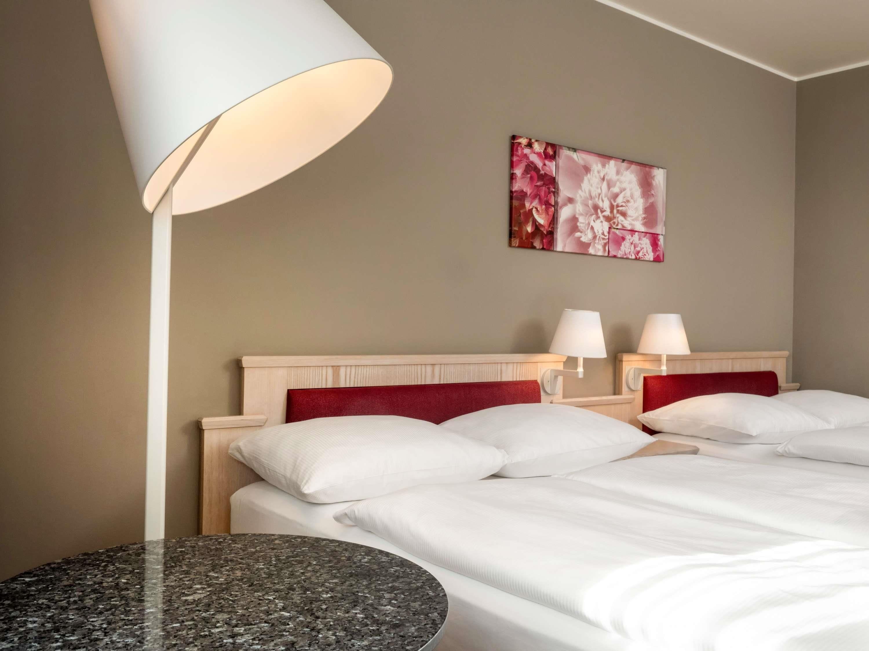 A hotel room with a bed, two bedside lamps, a round table, and a floral artwork on the wall.