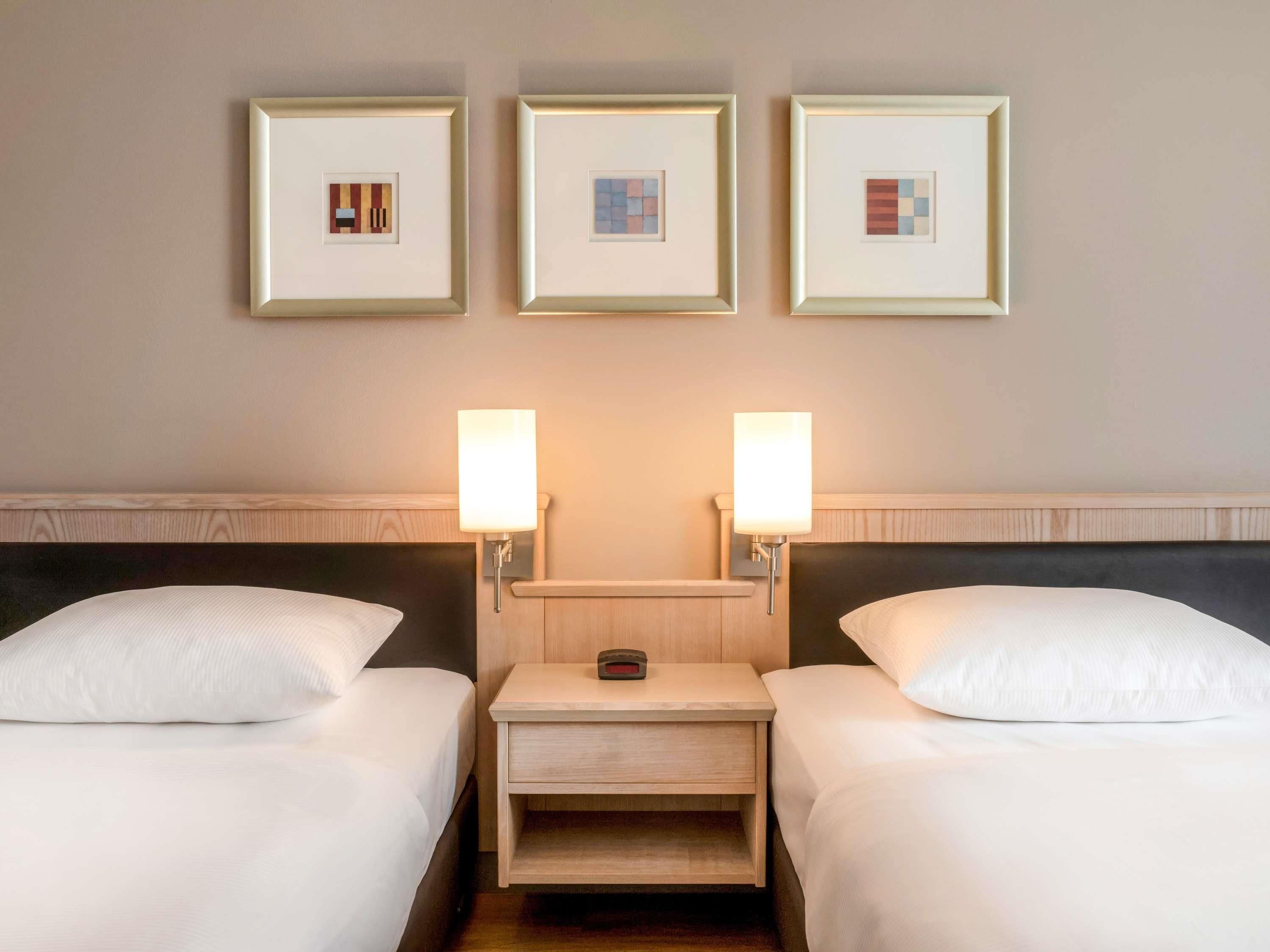 A hotel room with two beds, a nightstand, and three framed pictures on the wall.