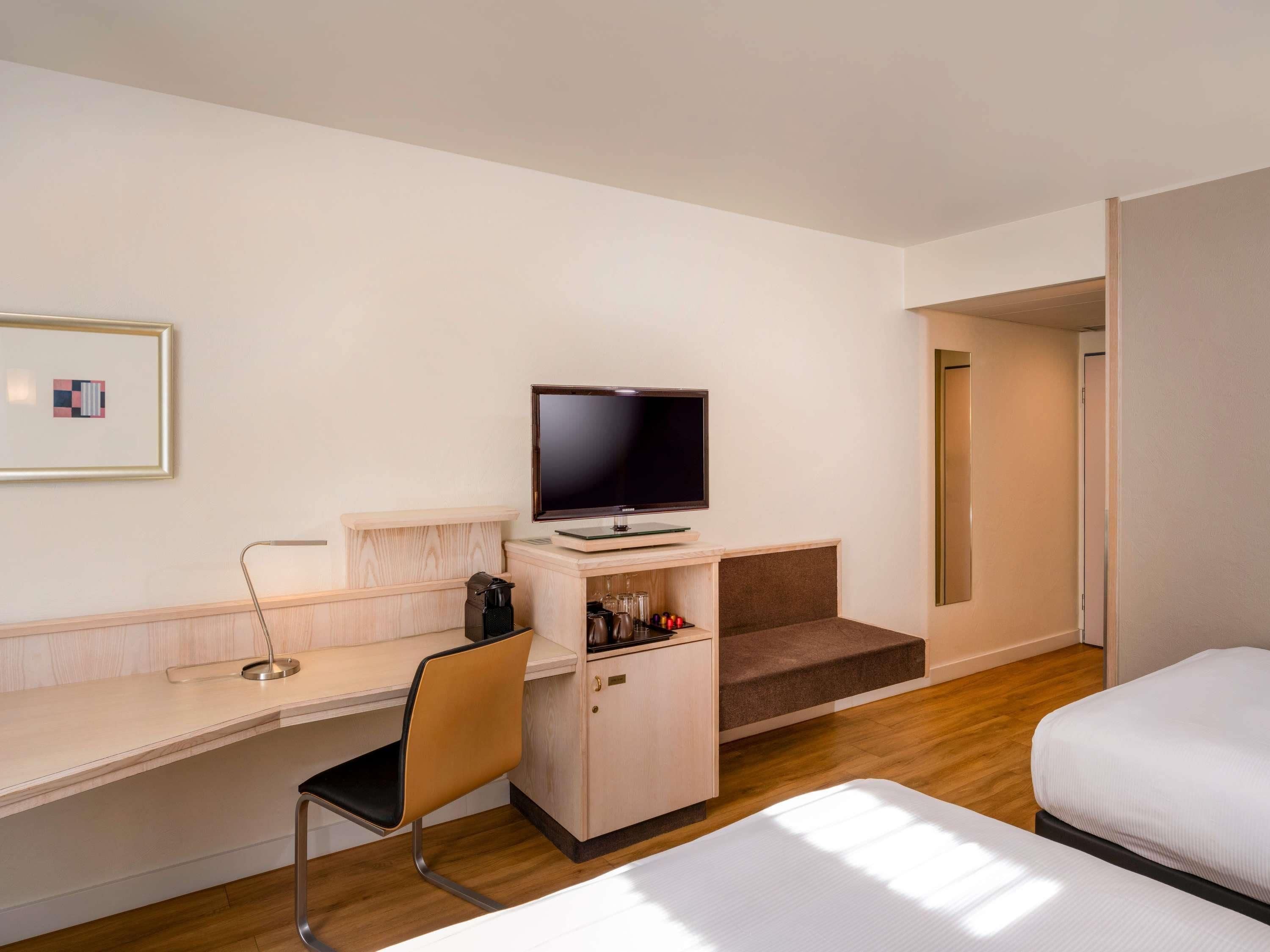 A hotel room with a bed, a desk with a chair, a television, and a coffee machine.