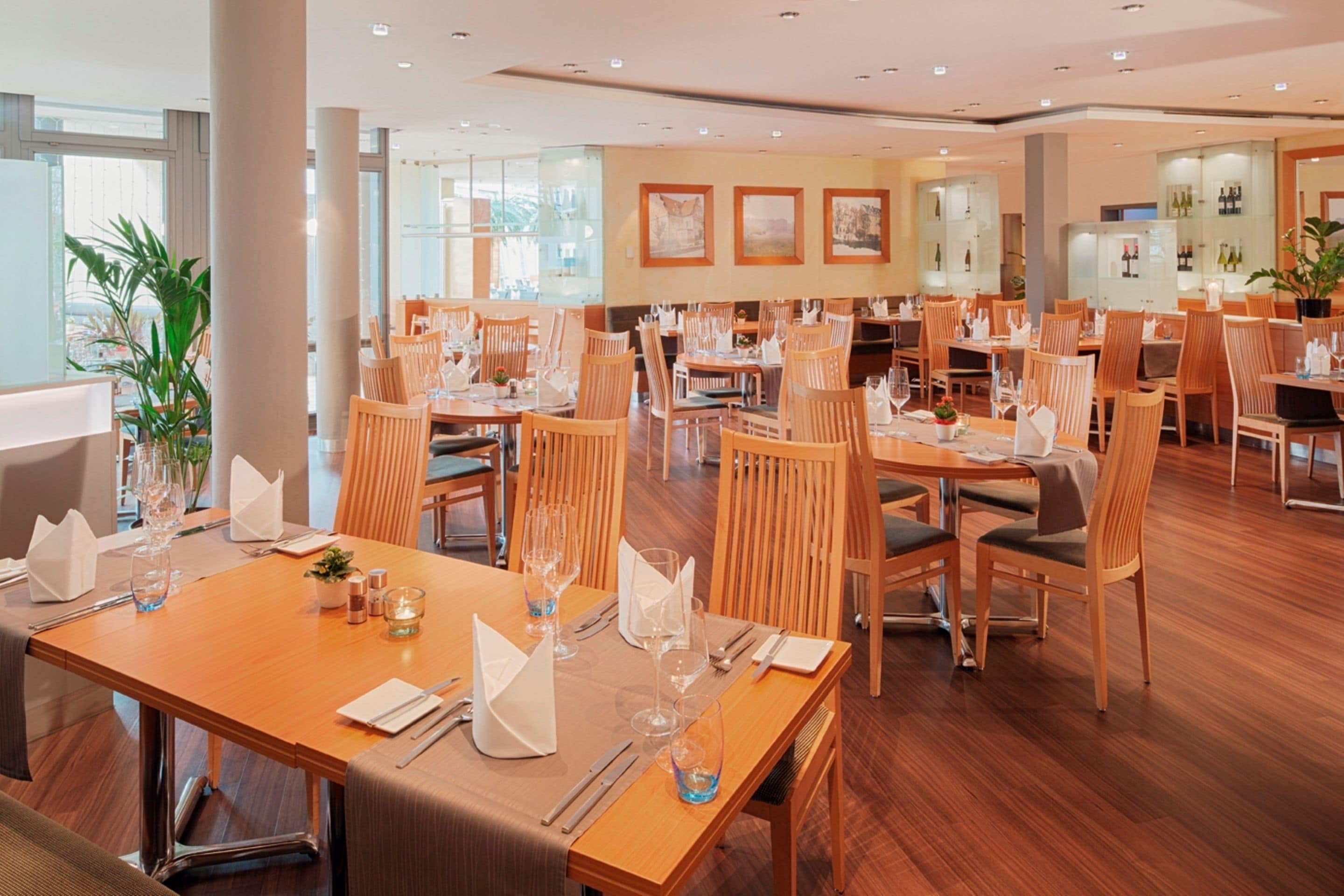 A spacious restaurant with multiple dining tables and chairs, large windows, and a modern interior design.