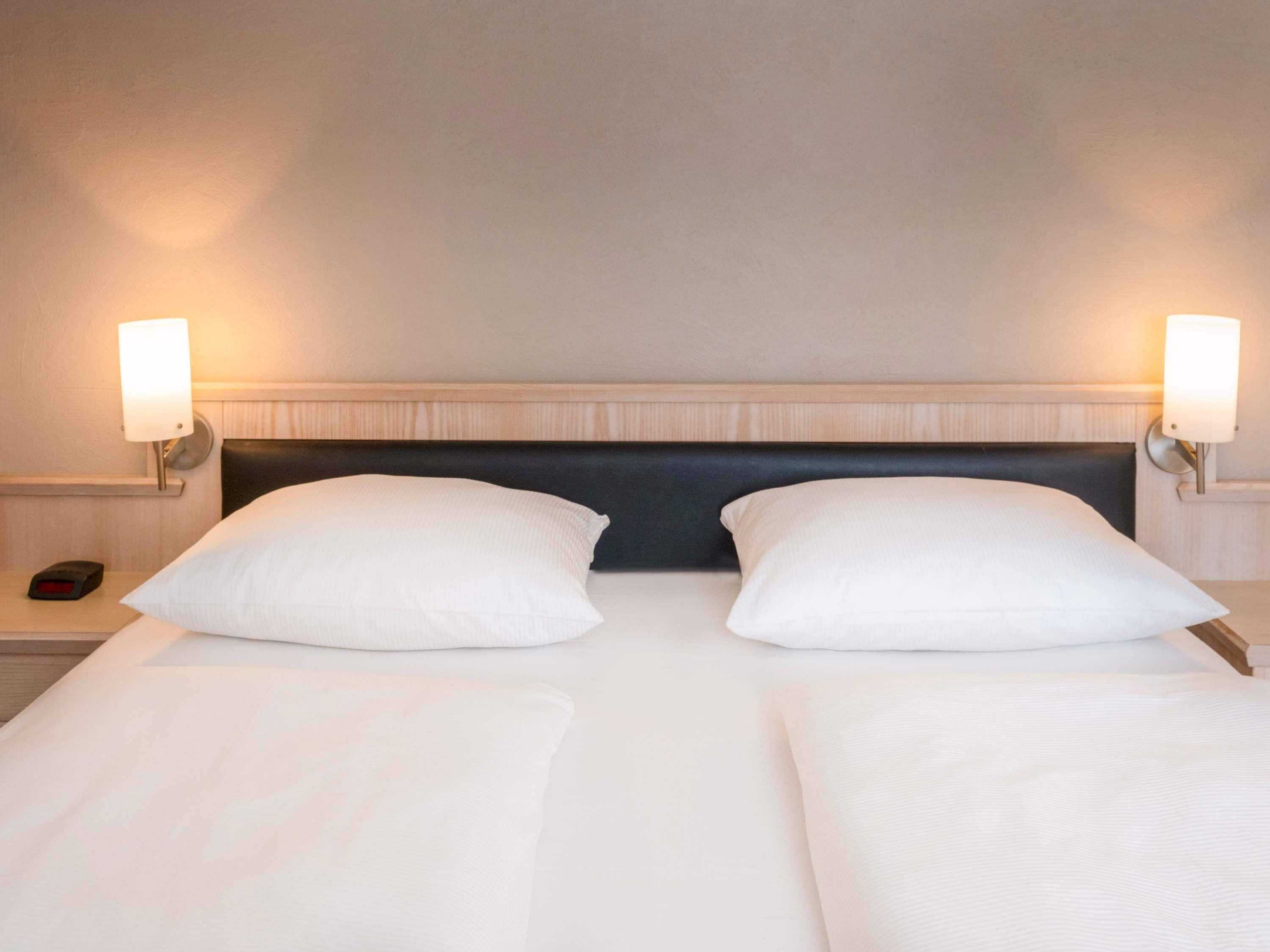 Een hotelkamer met een tweepersoonsbed, twee bedlampjes en een nachtkastje met een klok.