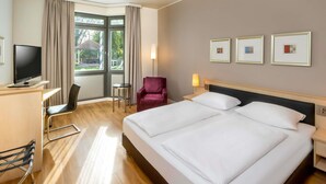 Een hotelkamer met een groot bed, een bureau met een televisie, een stoel, een tafeltje en een raam met gordijnen.