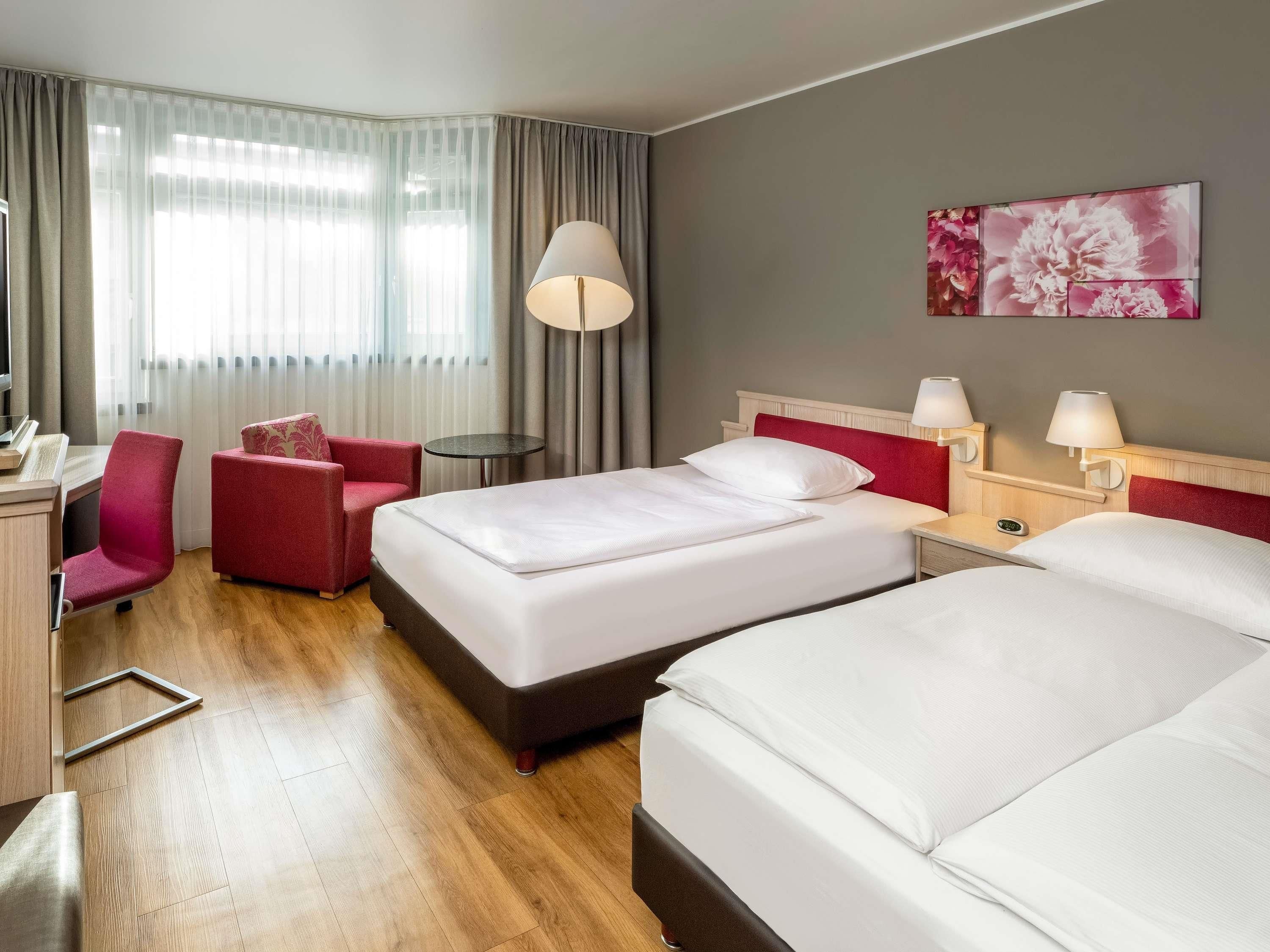 Een hotelkamer met twee bedden, een bureau, een stoel, een klein tafeltje en een lamp.
