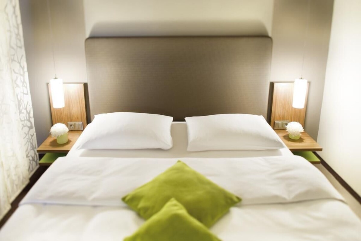 A hotel room with a bed, two bedside lamps, and a nightstand with a clock.