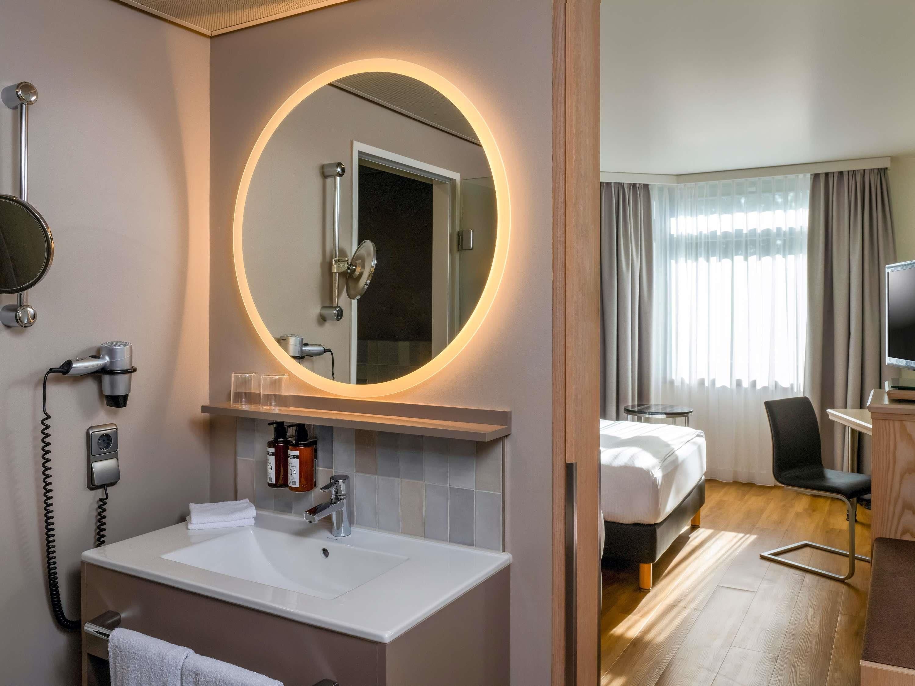 A hotel bathroom with a large mirror, a sink, a hairdryer, and a telephone.