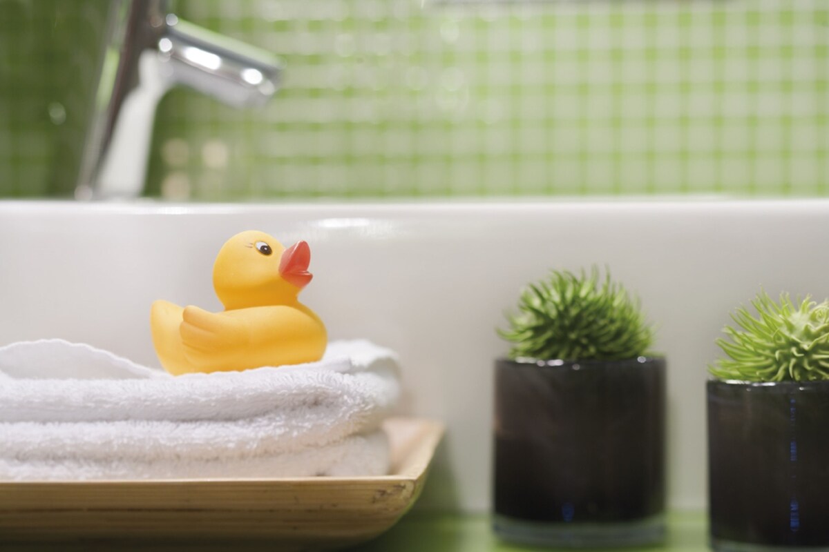 A bathroom with a bathtub, a rubber duck, a towel, and two potted plants.