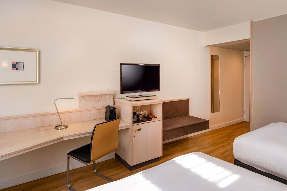 Ein Hotelzimmer mit Bett, Schreibtisch mit Stuhl, Fernseher und einer Kaffeemaschine.