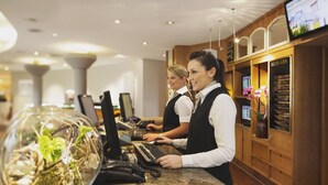 A reception area with two receptionists at a counter, a large aquarium, and a 'MESSAGES' sign. - Mövenpick Hotel München Airport (Hallbergmoos)