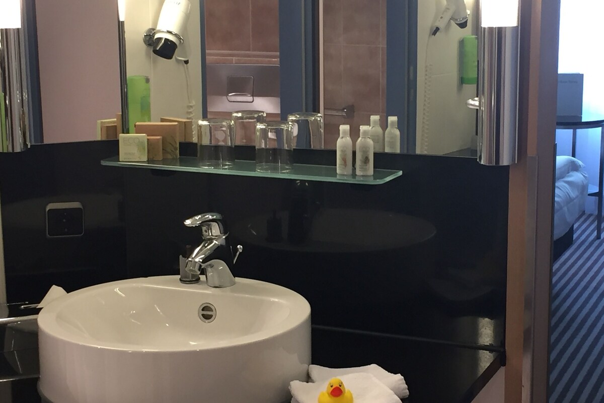 A bathroom with a white sink, a mirror, and toiletries on a shelf.