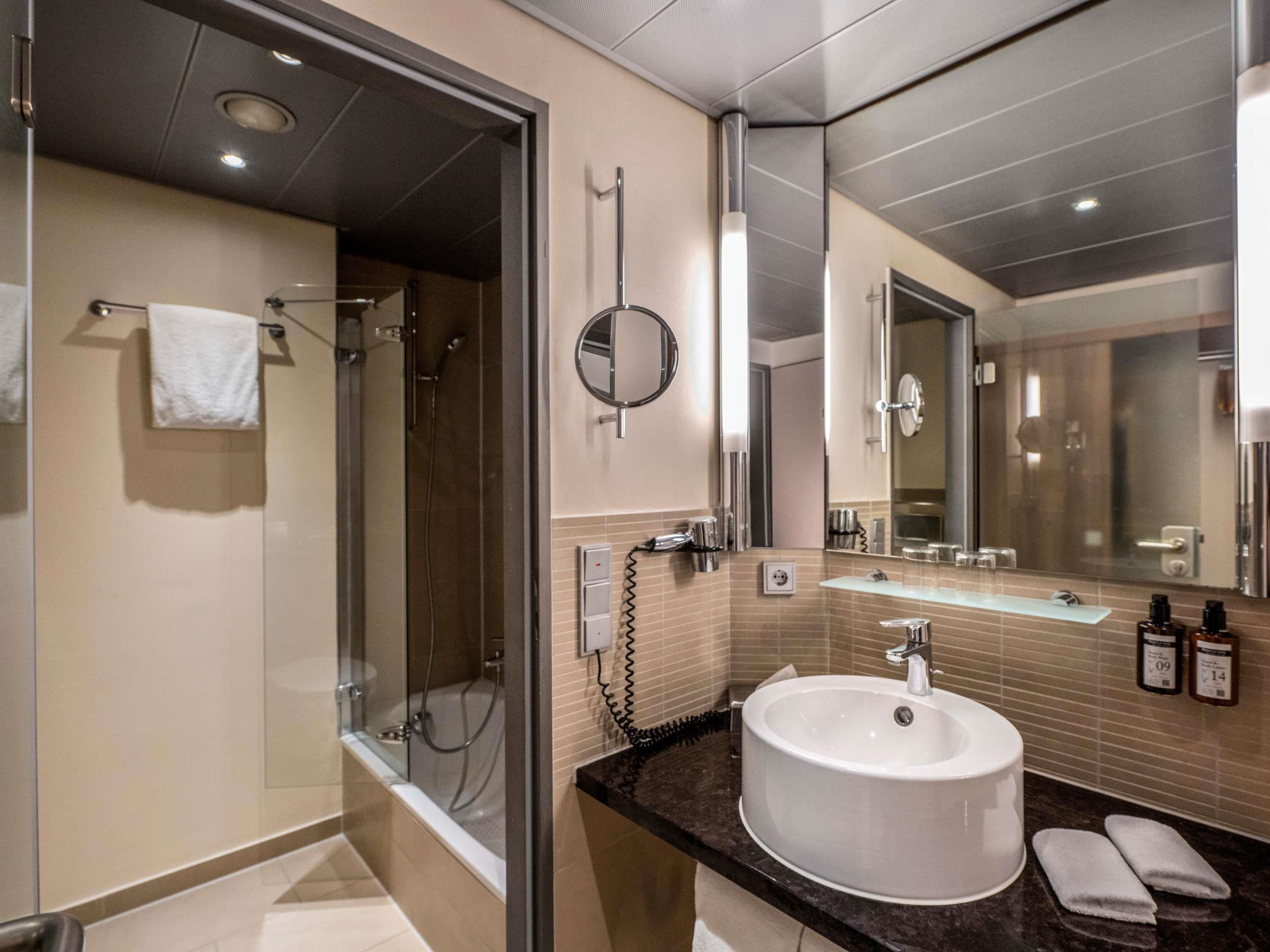 Une salle de bain moderne avec une douche à parois de verre, un grand miroir et un lavabo rond.
