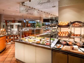 Uma área de buffet com diversas opções de comida, incluindo pão e doces, e um expositor de vidro.