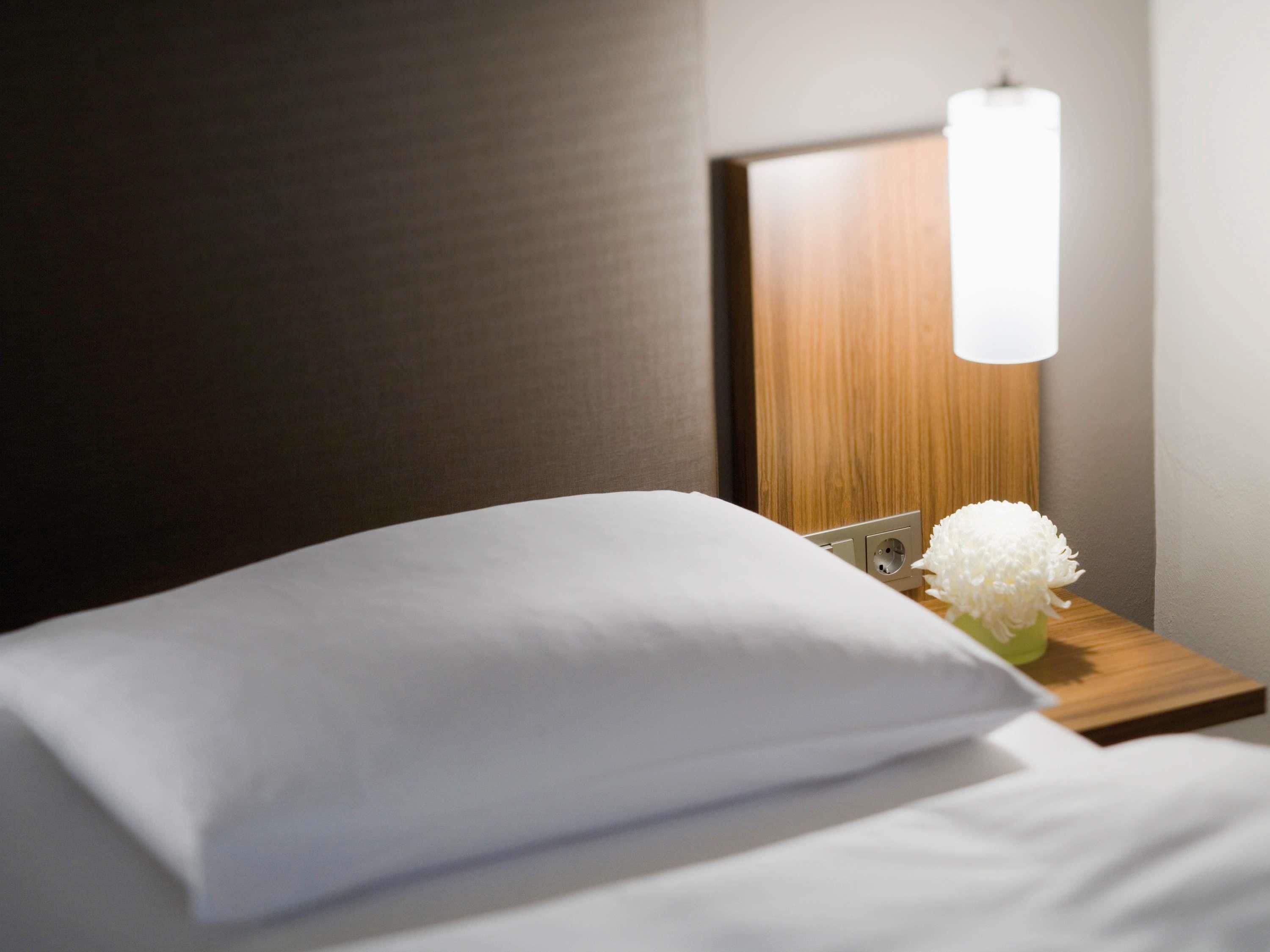 Una cama bien hecha con una almohada blanca y un pequeño jarrón con flores blancas.