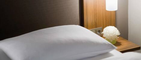 Una cama bien hecha con una almohada blanca y un pequeño jarrón con flores blancas.