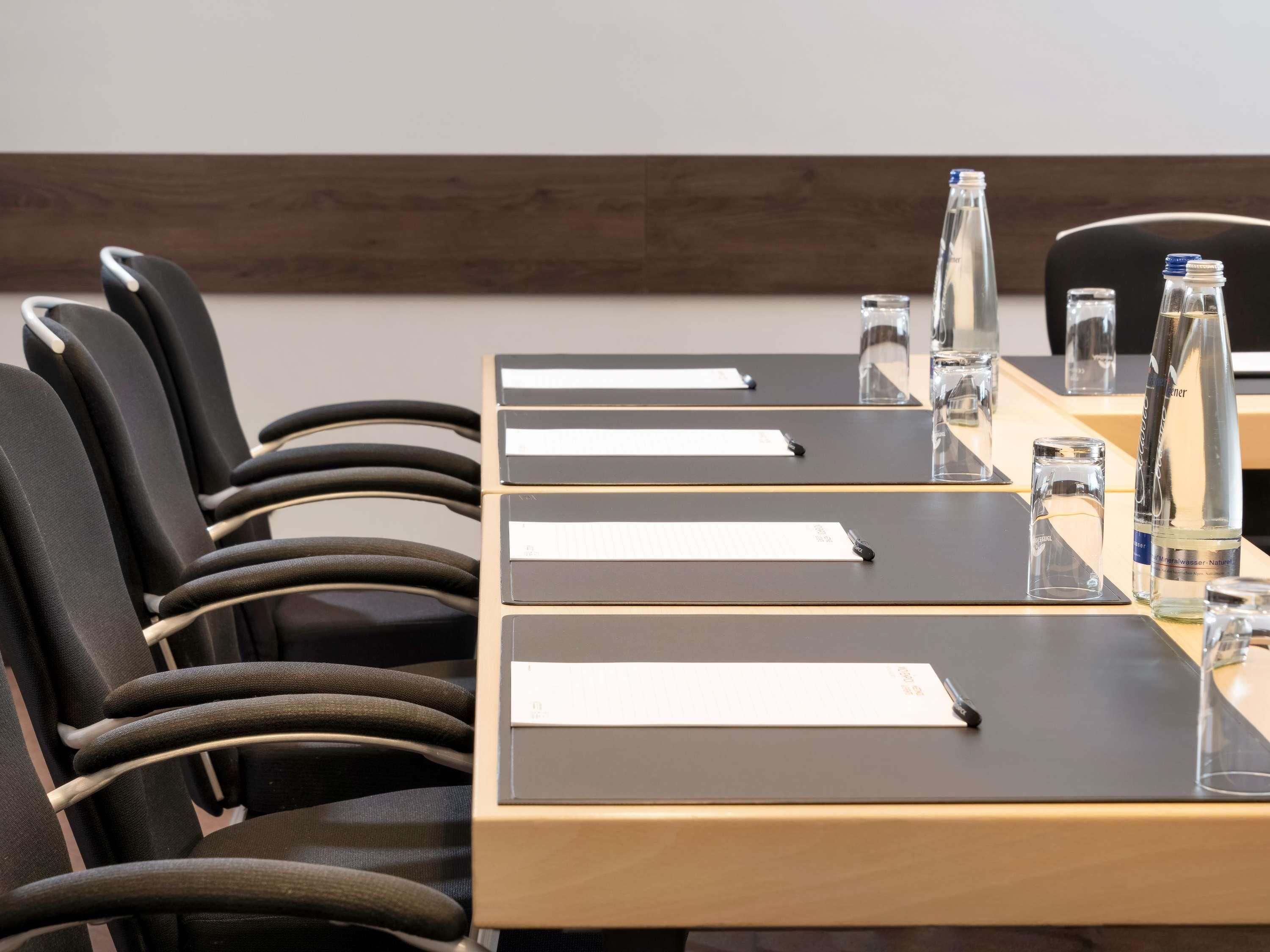 A conference room with a long table, black chairs, nameplates, water bottles, and glasses.