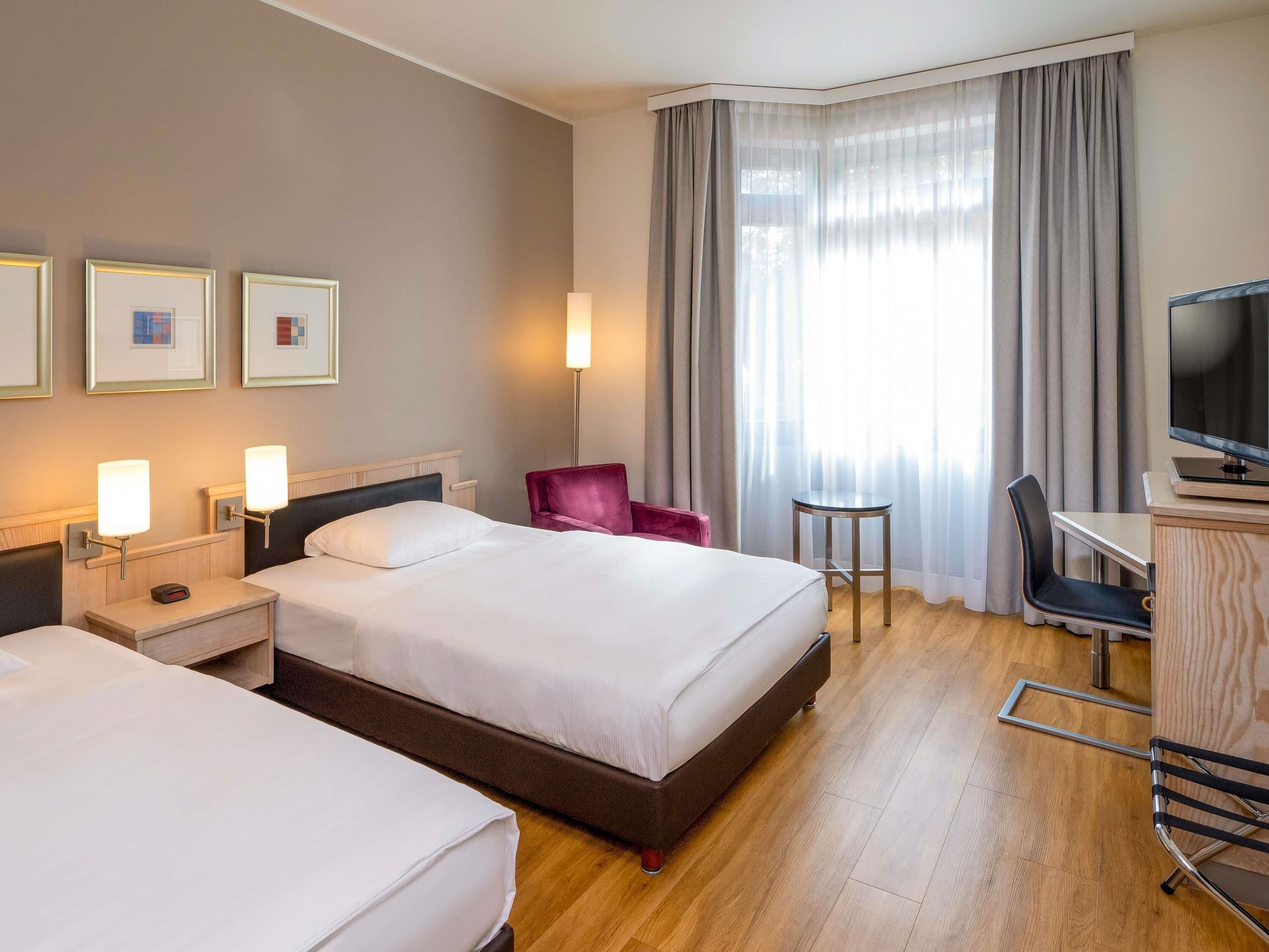 A hotel room with two beds, a desk with a chair, a TV, and a lamp.