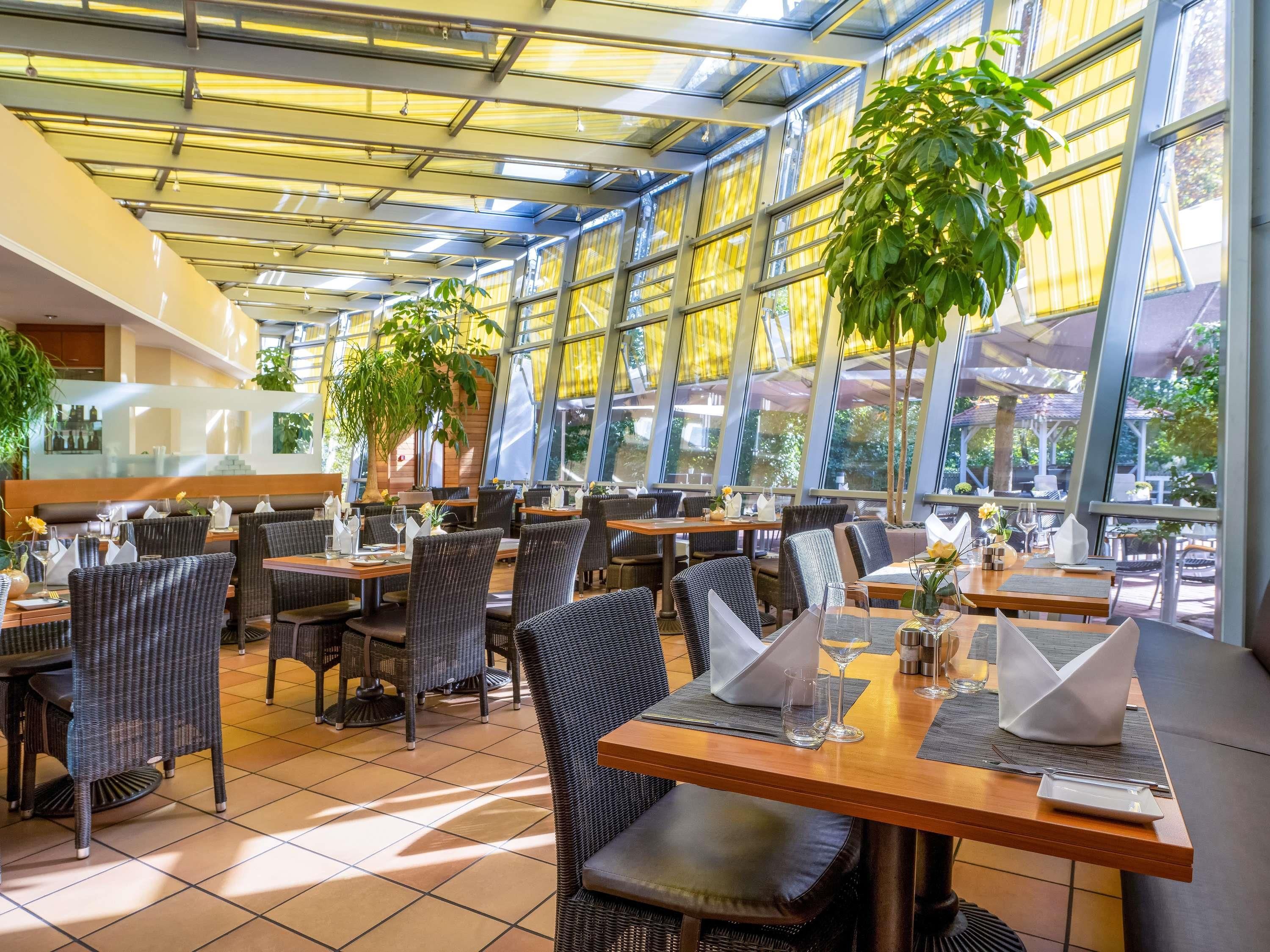 Un restaurante con mesas dentro, ventanales amplios y plantas en macetas.