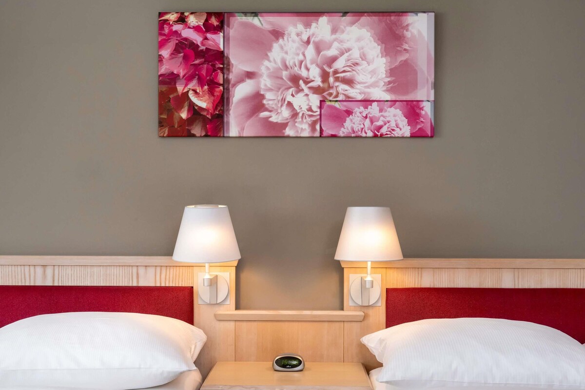 Een hotelkamer met twee bedden, een nachtkastje met een digitale klok en wandlampen.