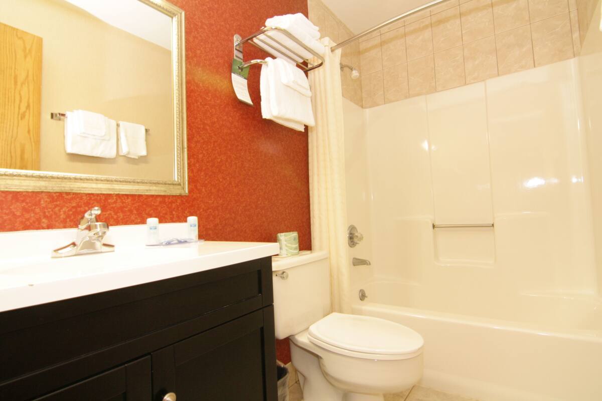 A bathroom with a white sink, mirror, and toilet. There is a towel rack with towels and a shower curtain.