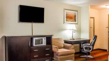 Habitación de hotel con cama, escritorio con computadora, silla, televisor, microondas y un cuadro en la pared.