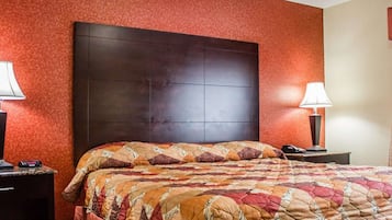 Quarto de hotel com uma cama grande, cabeceira escura, paredes vermelhas e duas luminárias de cabeceira.