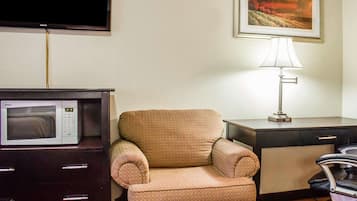 Habitación de hotel con un sillón marrón, un escritorio con lámpara, un televisor de pantalla plana y un microondas.