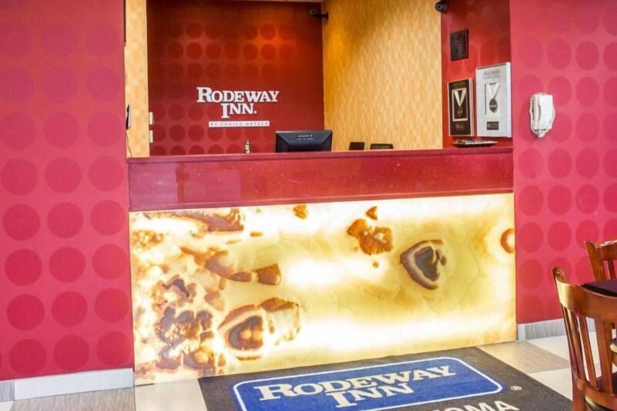 A reception desk at Rodeway Inn with a wooden counter and a sign above it.