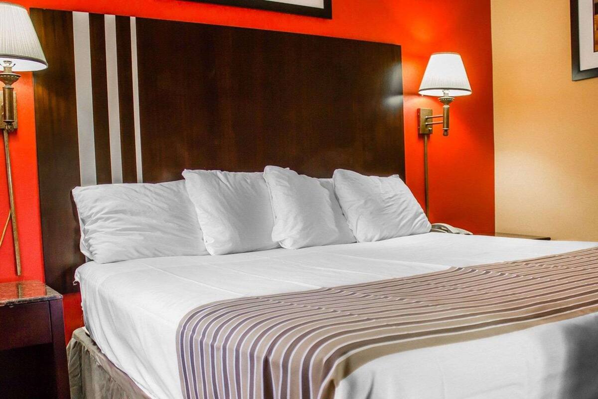A hotel room with a large bed, white bedding, and two wall-mounted lamps.