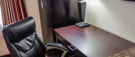 Habitación de hotel con una silla de cuero, un escritorio de madera, una lámpara y una pequeña mesa con encimera de granito.