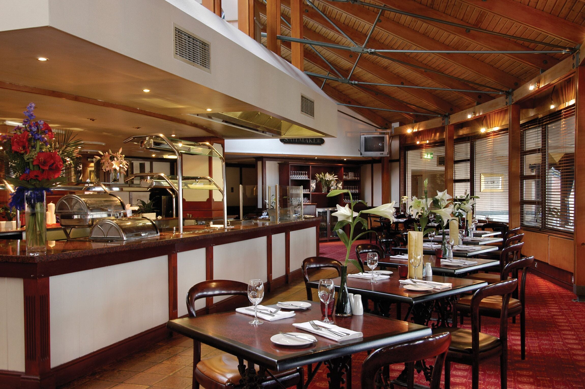 A restaurant with wooden furniture, a buffet area, and a high ceiling with exposed beams.