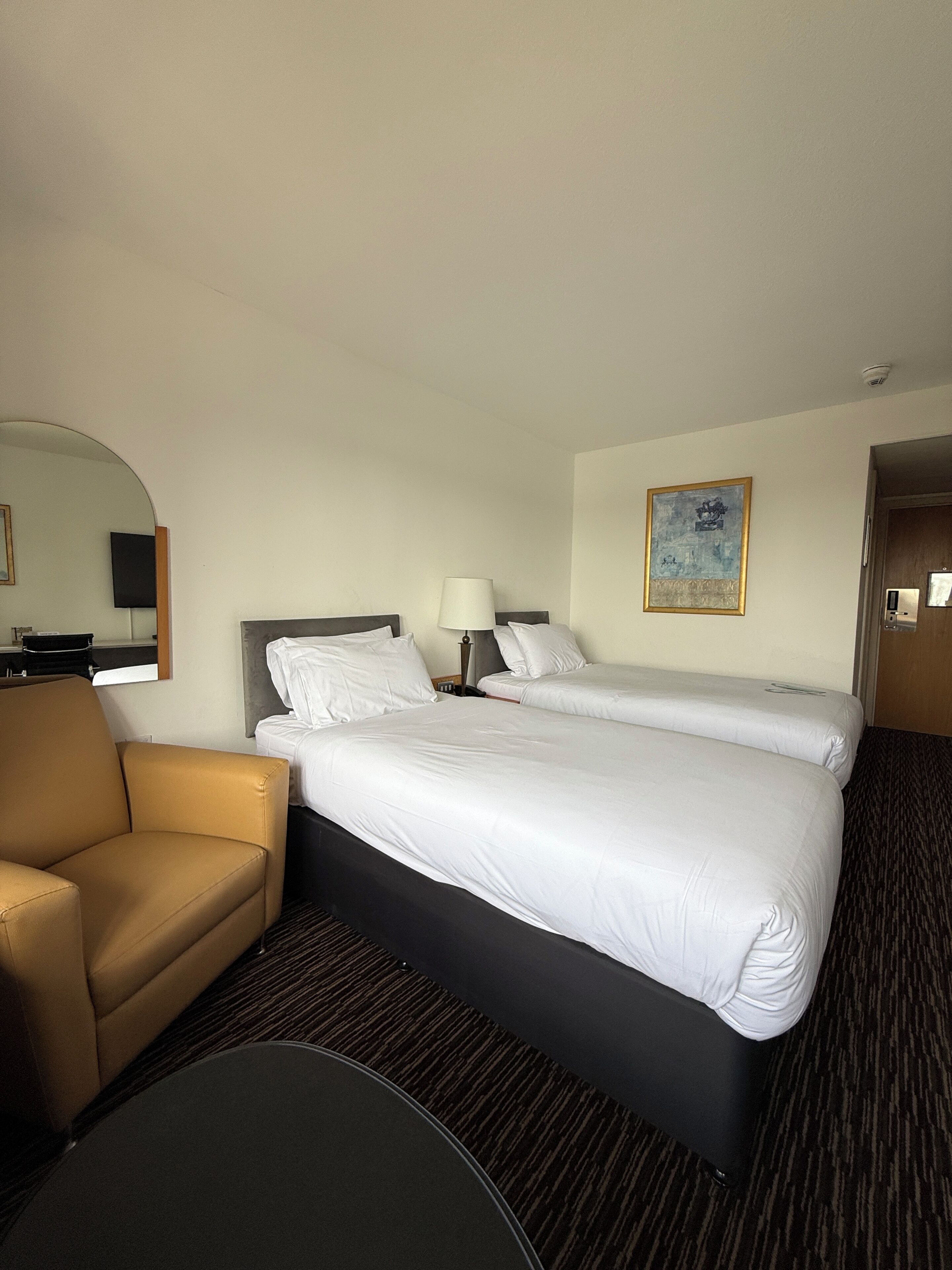 Habitación de hotel con dos camas, un sofá, un escritorio, una lámpara, un cuadro y un espejo.