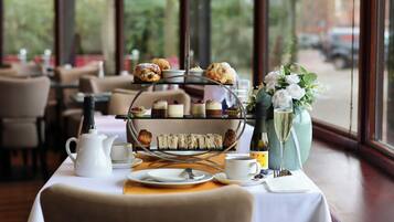 A table set for a tea service with a tiered display of pastries, a teapot, cups, and a vase with flowers.