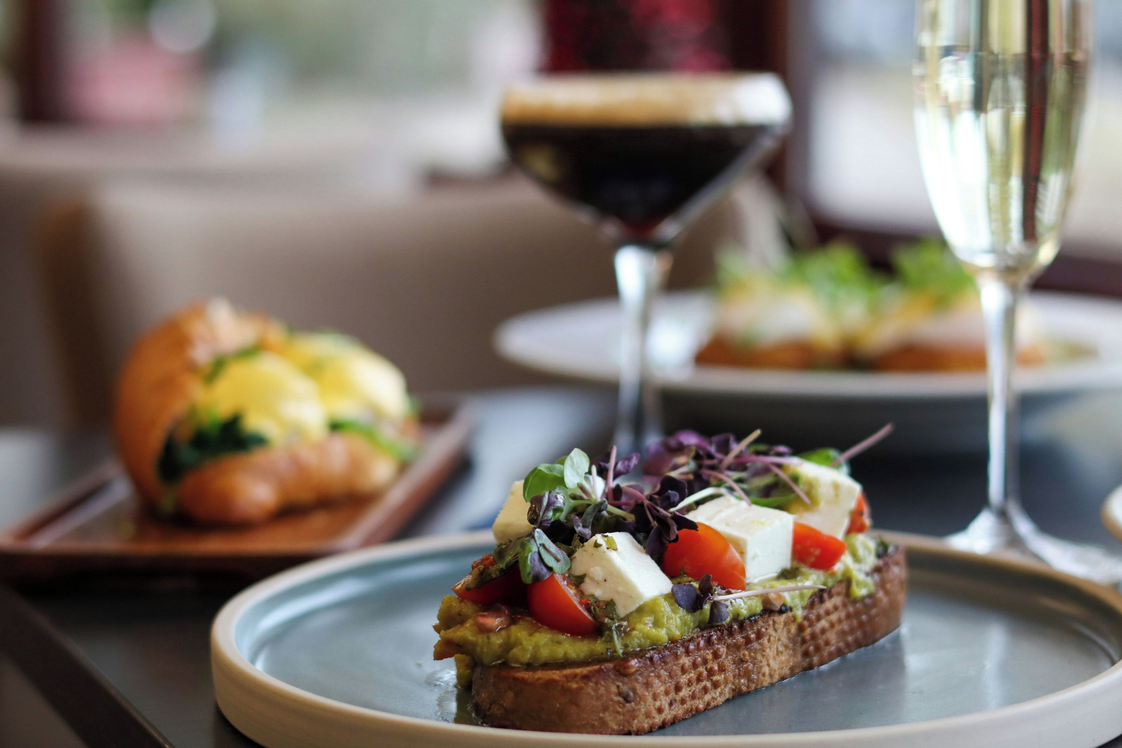 A plate with a sandwich topped with vegetables and cheese, a glass of red wine, and a blurred background.