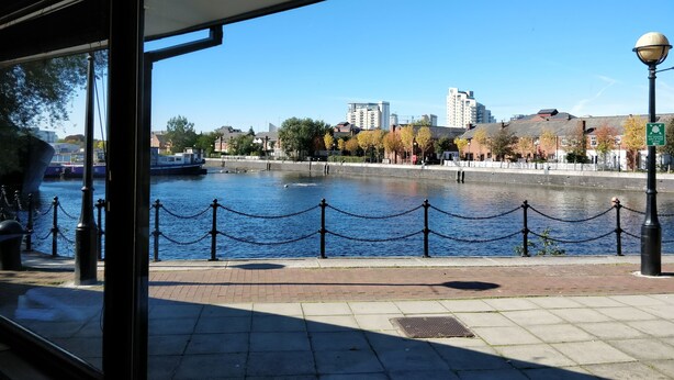 A riverside walkway with a chain barrier, a boat on the water, and buildings in the background. - Copthorne Hotel Manchester Salford Quays (Salford)