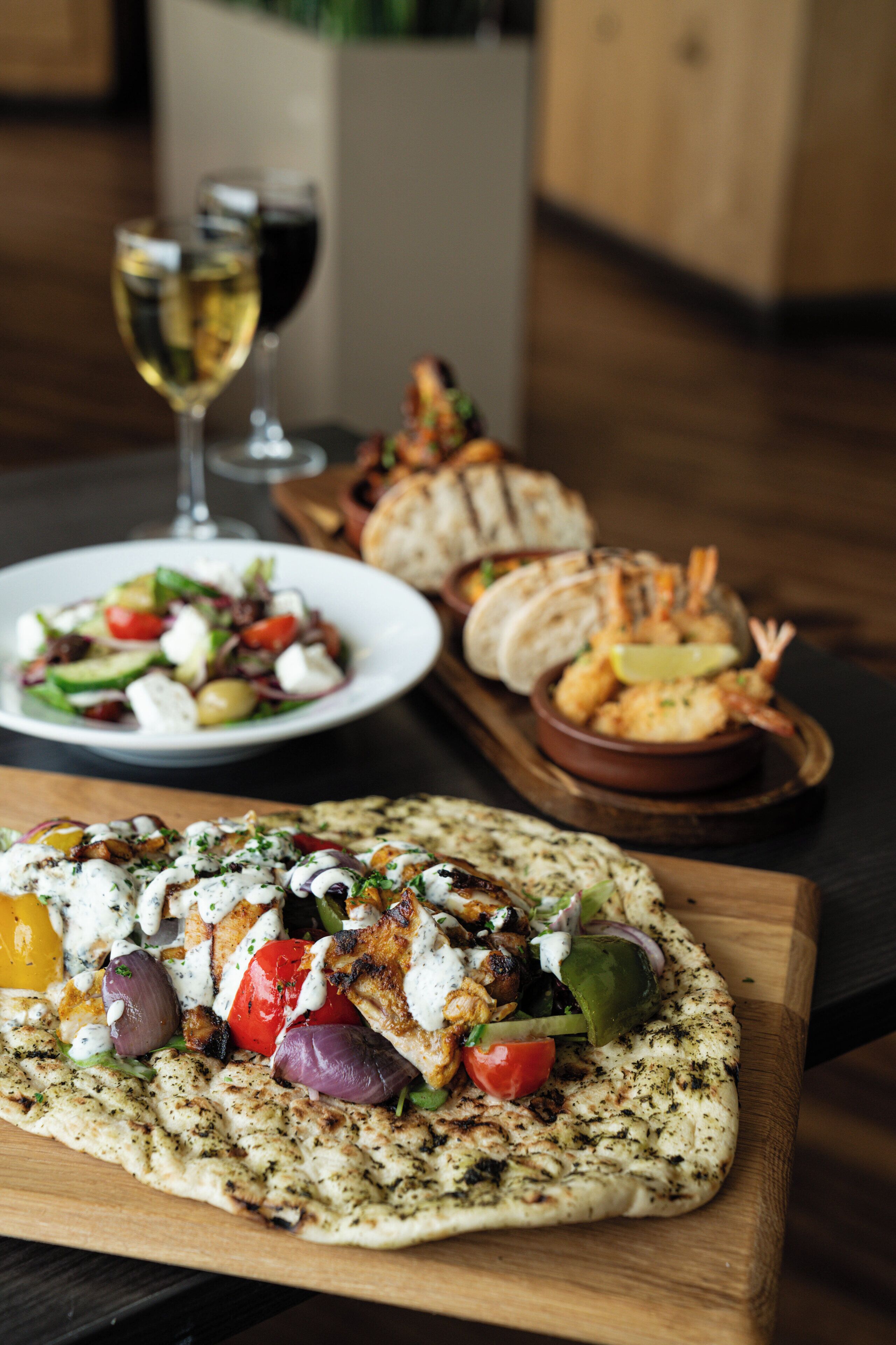 A wooden table with a pizza topped with vegetables and a bowl of shrimp.