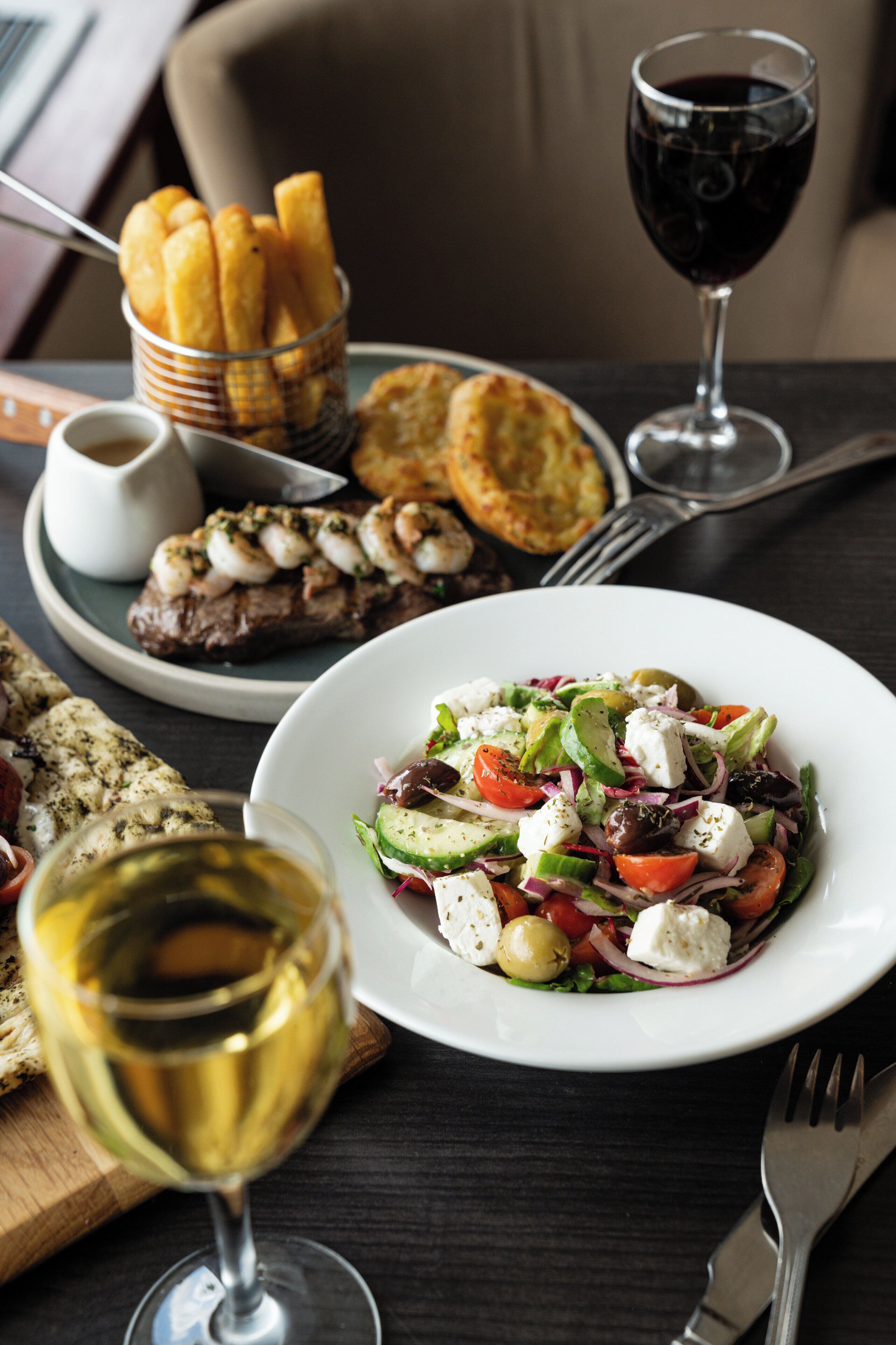 A dining table with a plate of salad, a glass of wine, a basket of breadsticks, and a small dish of sauce.